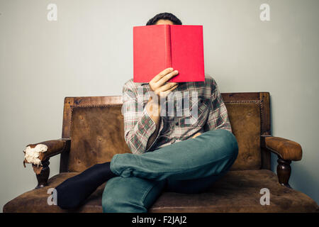 Giovane uomo seduto sul divano libro di lettura Foto Stock