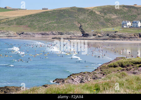 North Cornwall - Polzeath - la spiaggia dalle scogliere della baia - rottura top bianco onde - surfers - la luce del sole cielo blu + mare Foto Stock