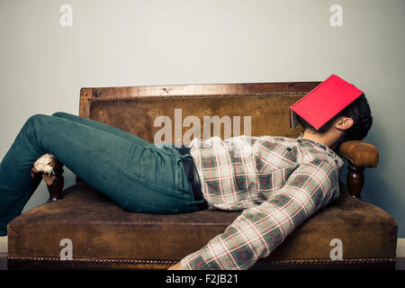 Giovane uomo che dorme sul divano con libro che copre il volto Foto Stock