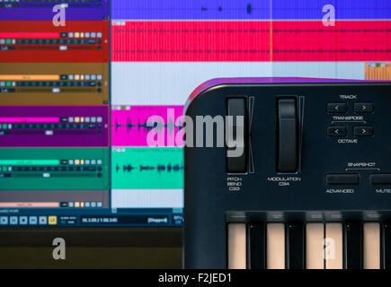Tastiera MIDI e controller con i fader e i pulsanti. Le forme d'onda in un DAW sono visibili in background Foto Stock