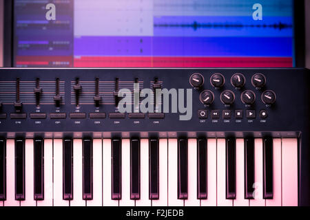 Tastiera MIDI e controller con i fader e i pulsanti. Le forme d'onda in un DAW sono visibili in background Foto Stock