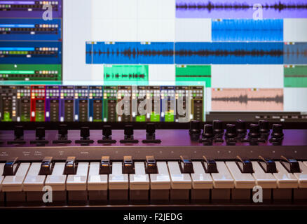 Tastiera MIDI e controller con i fader e i pulsanti. Le forme d'onda in un DAW sono visibili in background Foto Stock