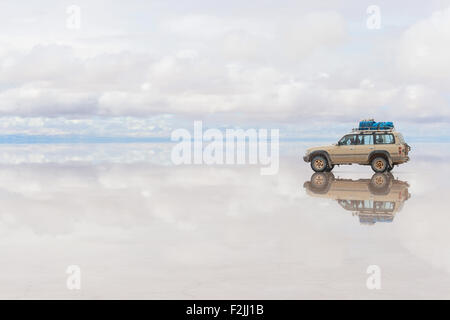 Off-road auto in movimento sulla superficie di riflessi del lago Salar de Uyuni in Bolivia Foto Stock