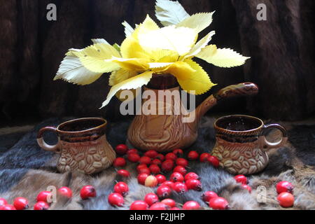 Bouquet luminoso di fogliame giallo soggiorno in vaso di argilla con due tazze marrone sul pelo con red bacche mature di biancospino Foto Stock