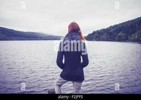 Giovane donna in piedi dal lago sul giorno di autunno Foto Stock