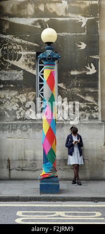 Una giovane donna e il suo telefono cellulare accanto a un allegramente vestita lampada posta su Nelson Street nel centro città di Bristol REGNO UNITO Foto Stock