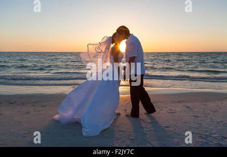 Una coppia sposata, la sposa e lo sposo che si baciano al tramonto o l'alba su una bella spiaggia tropicale Foto Stock