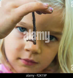 Bambino ragazza bionda holding lombrico fuori in giardino, ritratto, estate, mano, backyard, natura Foto Stock