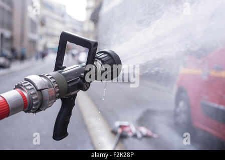 Acqua spruzzi a getto da una lotta antincendio firehose ugello con un rosso fuoco fighter carrello a Parigi Foto Stock