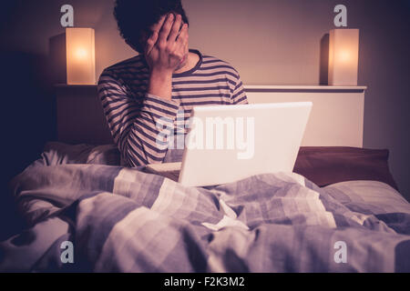 Uomo con notebook facepalming nel letto di notte Foto Stock