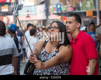 Una giovane coppia prende un selfie con un bastone selfie durante la visita a Times Square a New York City. Foto Stock