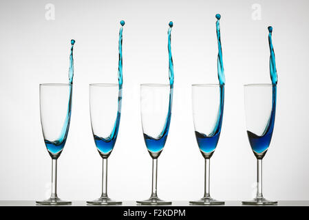 Cinque flauti champagne con colore blu di spruzzi di liquido. Alta velocità flash fotografia Foto Stock