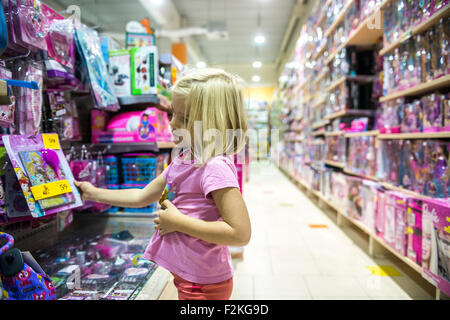 Bambino ragazza bionda scegliendo e shopping un giocattolo nel negozio di giocattoli Foto Stock