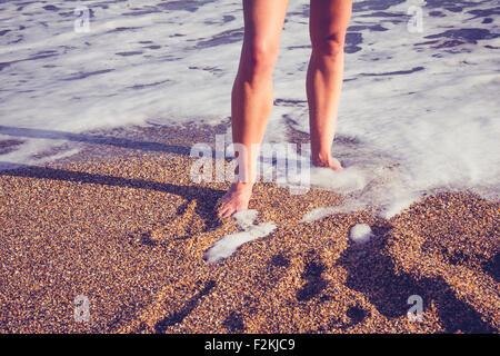 Giovane donna è la gamba nel surf sulla spiaggia Foto Stock