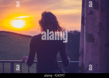 Giovane donna ammirando il tramonto dal suo balcone Foto Stock