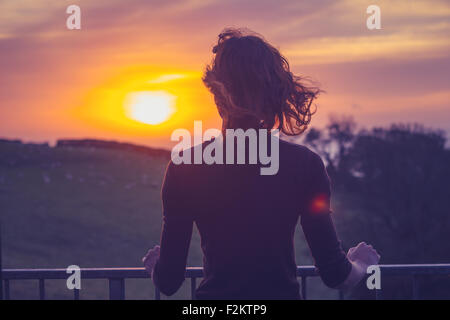 Giovane donna ammirando il tramonto dal suo balcone Foto Stock