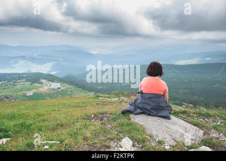 La Bulgaria, Rila montagne, vista posteriore del senior donna seduta su una roccia a guardare view Foto Stock