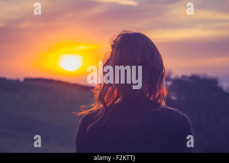 Giovane donna ammirando il tramonto sopra i campi Foto Stock