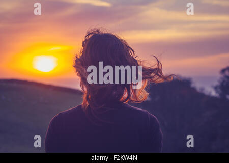 Giovane donna ammirando il tramonto sopra i campi Foto Stock