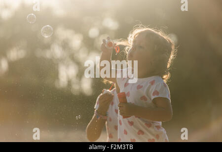 Due piccole sorelle rendendo le bolle di sapone nel parco al crepuscolo Foto Stock