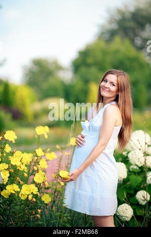 Donna incinta in posa di un giardino verde Foto Stock