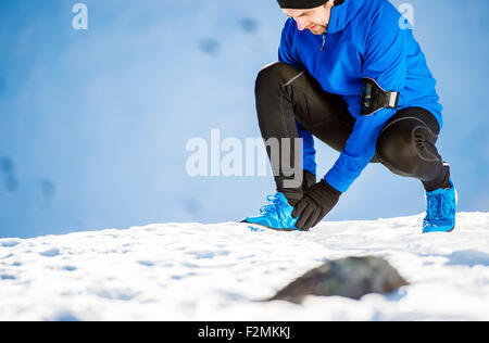 Giovane uomo avente uno zio pregiudizio durante il jogging al di fuori in inverno pieno di sole montagne Foto Stock