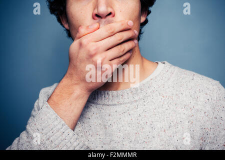 Giovane uomo che copre la bocca in stato di shock Foto Stock