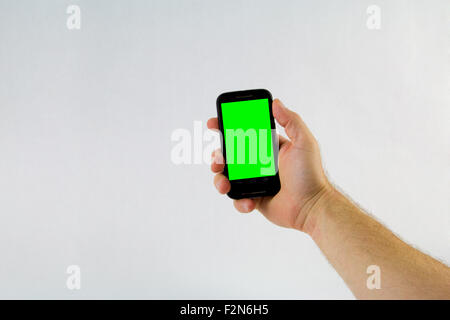 Maschio di mano azienda telefono cellulare su sfondo bianco con schermo verde Foto Stock