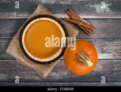 Torta di zucca con zucca e bastoncini di cannella contro la tavola in legno rustico Foto Stock