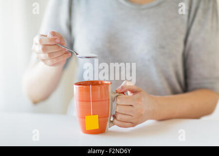 Close up di donna con aggiunta di zucchero per tazza da tè Foto Stock