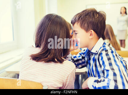 Sorridente schoolgirl whispering a classmate orecchio Foto Stock