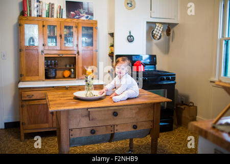 Caucasian baby ragazza seduta sul tavolo della cucina Foto Stock