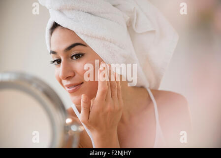 Donna con capelli in asciugamano lozione di sfregamento sulla faccia Foto Stock