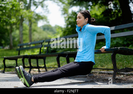 Donna ispanica facendo push-up su una panchina nel parco Foto Stock