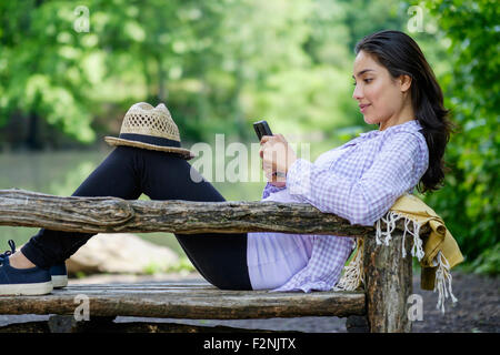 Donna ispanica tramite telefono cellulare su una panchina nel parco Foto Stock
