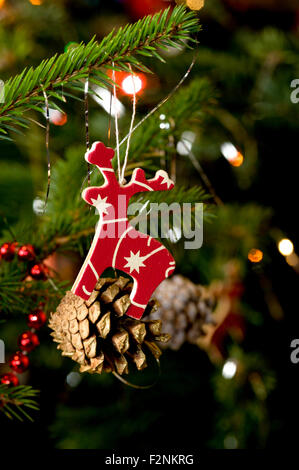 Un colorato in legno pitturato la figura a forma di renna appeso ad un pino tradizionale albero di natale Foto Stock