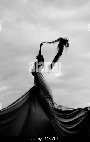 La donna caucasica fa roteare in tessuto sotto le nuvole Foto Stock