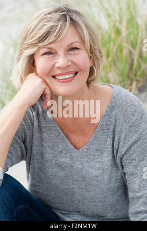 Sorridente Caucasian donna seduta sulla spiaggia Foto Stock