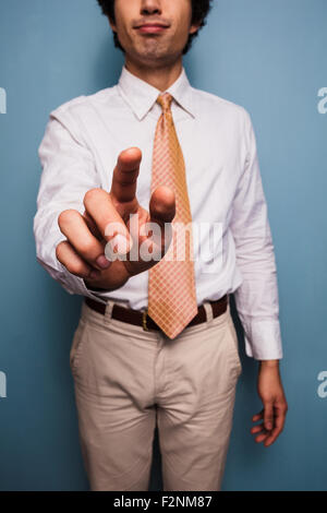 Giovane uomo in piedi da una parete blu e spingendo il pulsante immaginario Foto Stock
