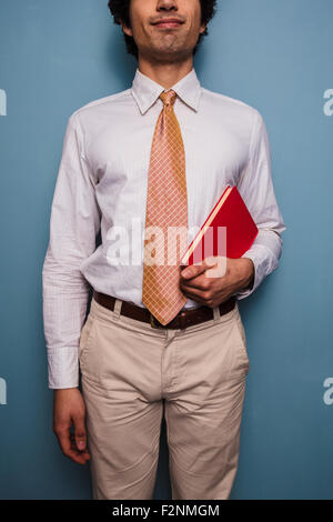 Giovane uomo in piedi da una parete blu con un libro rosso Foto Stock