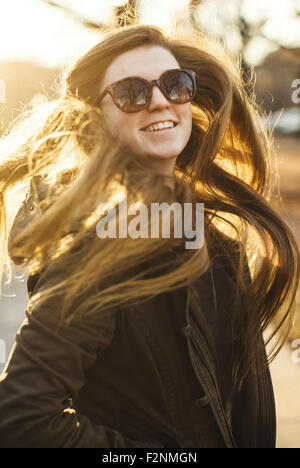 Sorridente donna caucasica nel lanciare i suoi capelli all'aperto Foto Stock