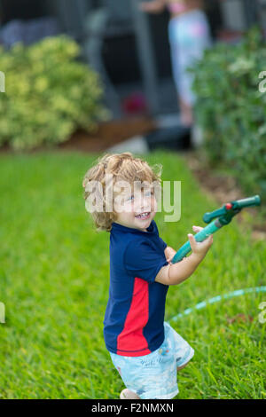 Caucasian baby boy giocando con il tubo flessibile nel cortile posteriore Foto Stock