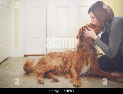 La donna caucasica baciare cane sul pavimento Foto Stock