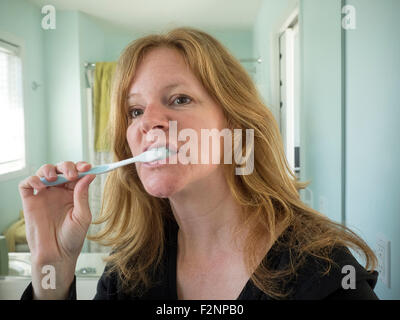 La donna caucasica spazzolare i suoi denti nella stanza da bagno Foto Stock