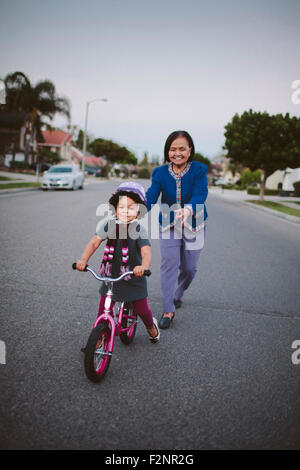 Nonna nipote di insegnamento per guidare la bicicletta sulla strada suburbana Foto Stock