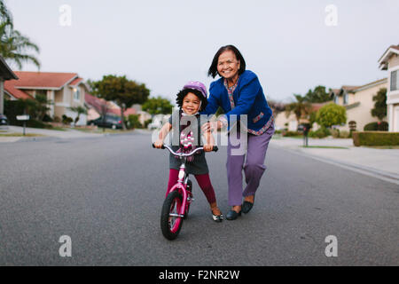 Nonna nipote di insegnamento per guidare la bicicletta sulla strada suburbana Foto Stock