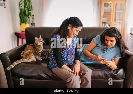 Ispanico madre e figlia tramite telefono cellulare sul divano Foto Stock