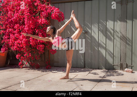 La donna a praticare yoga vicino a fiori e una recinzione Foto Stock