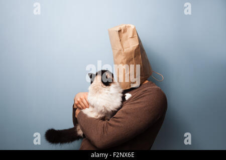 Un uomo con un sacchetto di carta sulla sua testa è in possesso di un confuso cat. Foto Stock