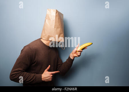 Un giovane uomo con un sacchetto di carta sulla sua testa è rivolta verso una banana come se si trattasse di una pistola! Foto Stock